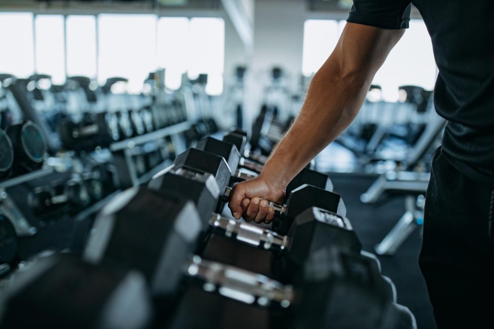 Homme prenant une haltère dans un rack de poids à l’intérieur d’une salle de sport.